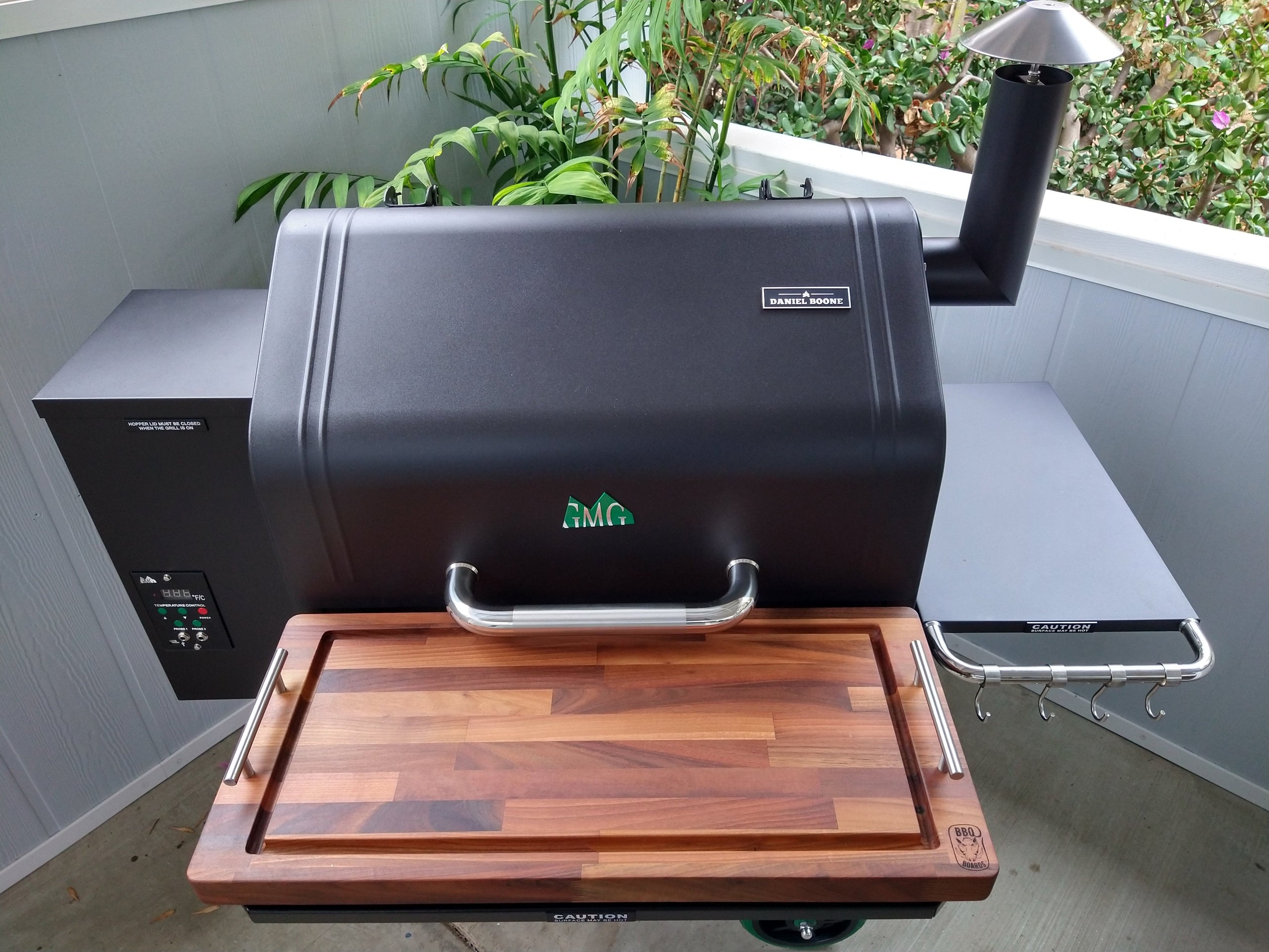 Black barbecue grill with a wooden cutting board on a patio