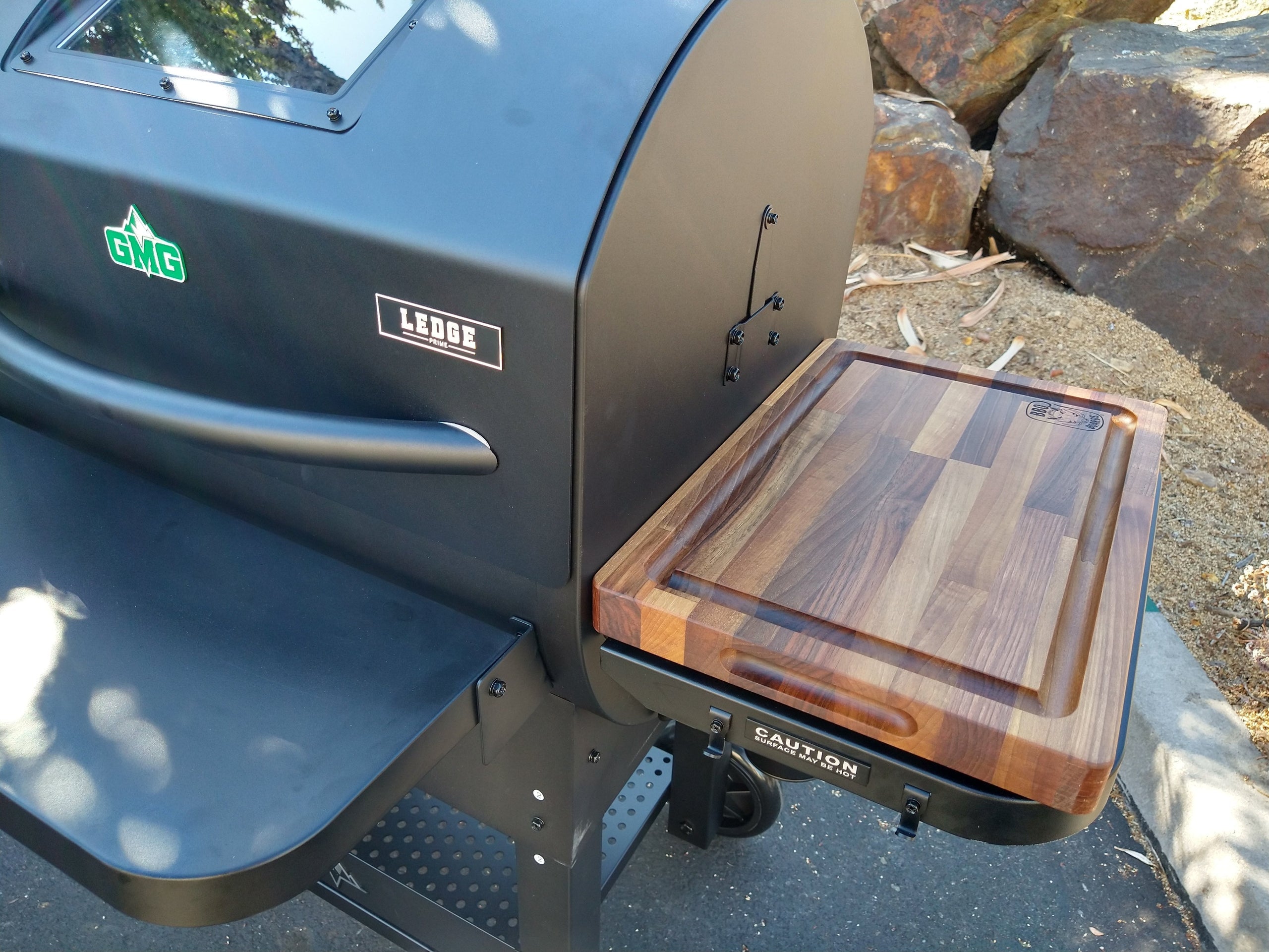 Outdoor grill with a wooden cutting board attached, featuring the brand 'Lodge'.